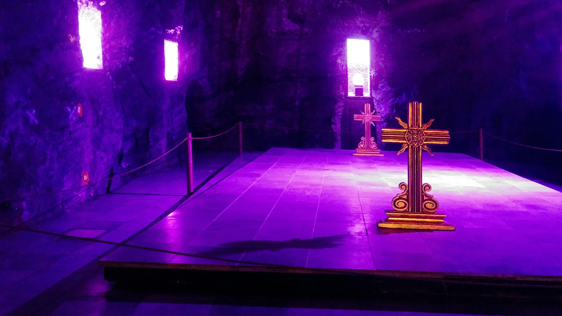 Two illuminated crosses standing inside the Salt Cathedral of Zipaquirá, carved salt walls lit in violet on either side