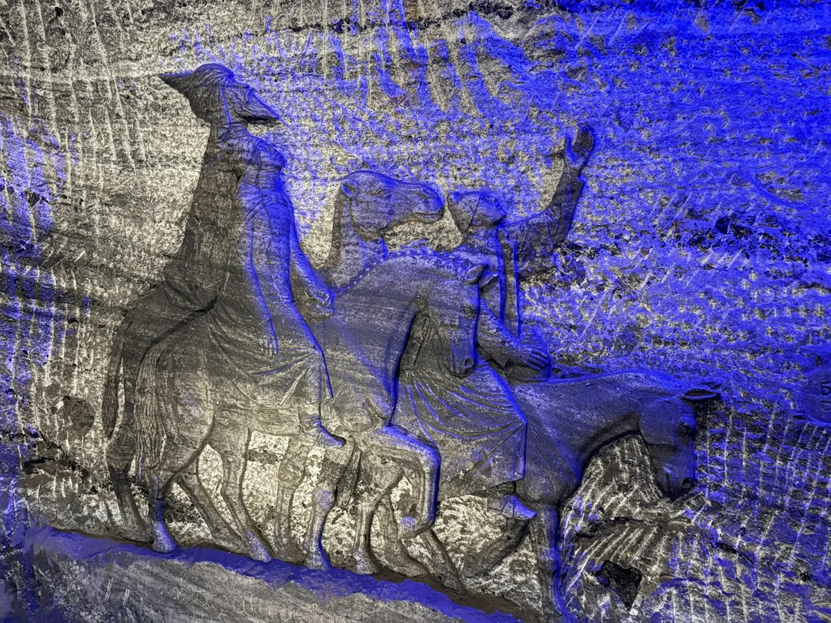 A scene carved in relief directly into the salt rock, lit in blue, showing robed figures on camels and horses